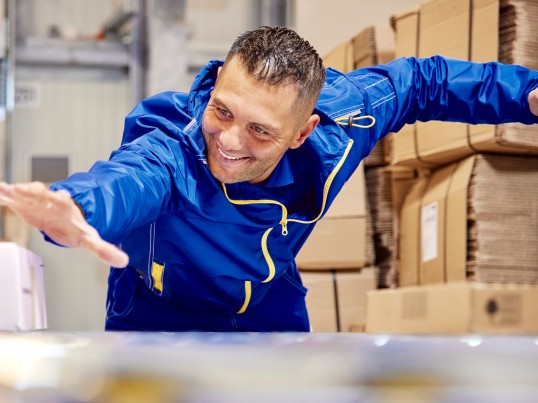 A GLS employee is sliding a parcel on the parcel conveyor belt.