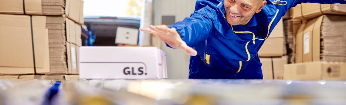 A GLS employee is sliding a parcel on the parcel conveyor belt.