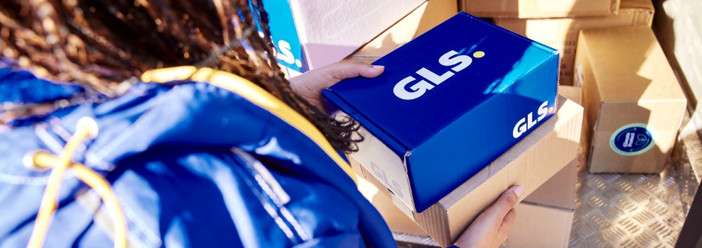GLS driver photographed from behind holding GLS parcels in her hands, and the parcels are on board the GLS van