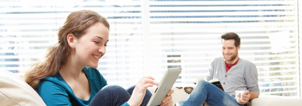 A woman using a tablet and a man reading a book while sitting on a couch.